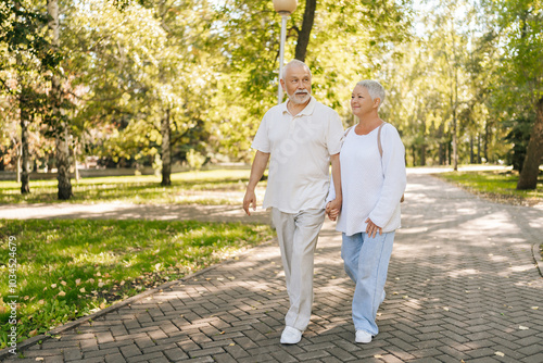Obraz na plátně Full length portrait of senior couple enjoying leisurely stroll in green park, holding hands intertwined, sharing tender moment on sunny day