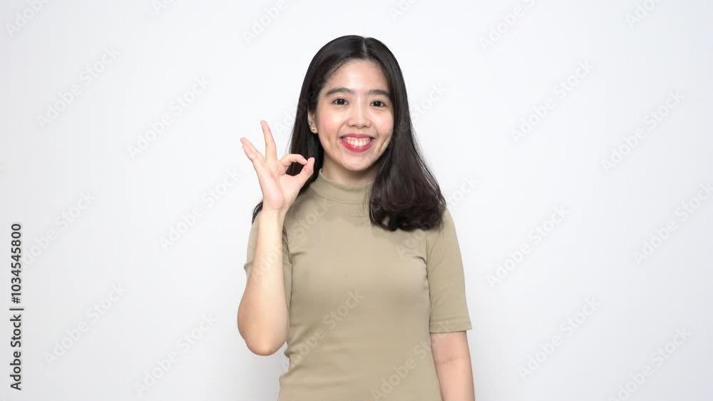 Beautiful Asian woman makes an 'okay' hand sign, expressing approval against a plain white background Beautiful Asian woman makes an 'okay' hand sign, expressing approval against a plain white background