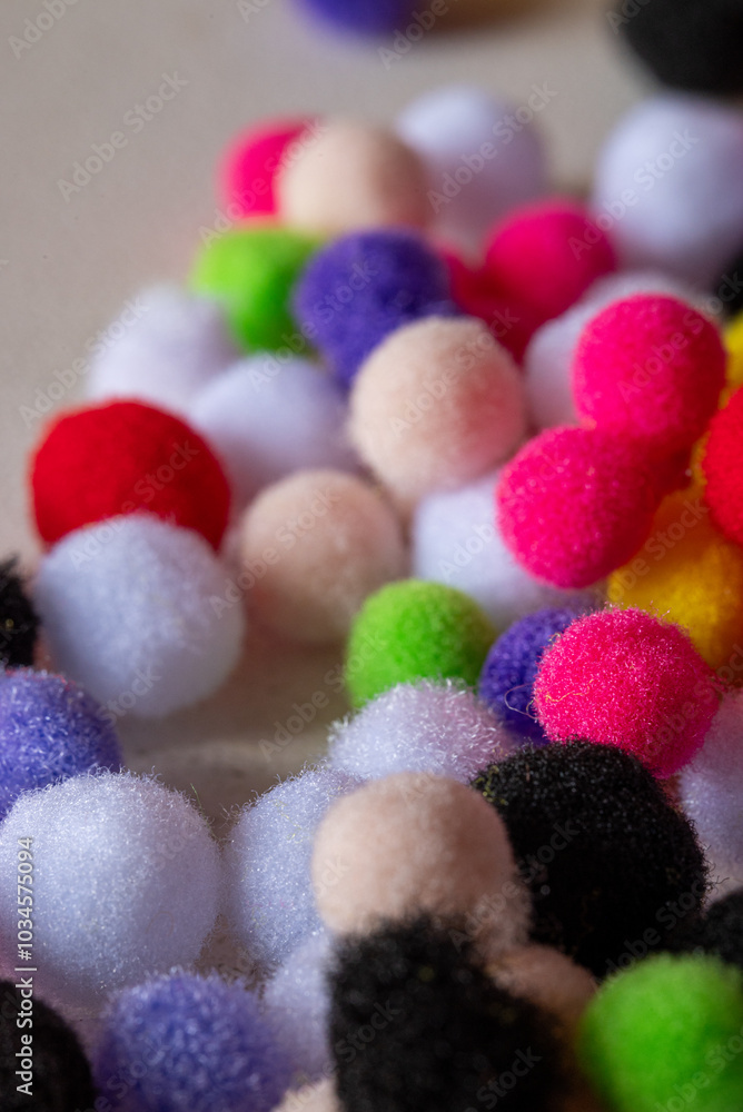 A pile of colorful pom poms are scattered on a table. The pom poms are of various sizes and colors, including red, green, yellow, and purple. Concept of playfulness and creativity A pile of colorful pom poms are scattered on a table. The pom poms are of various sizes and colors, including red, green, yellow, and purple. Concept of playfulness and creativity