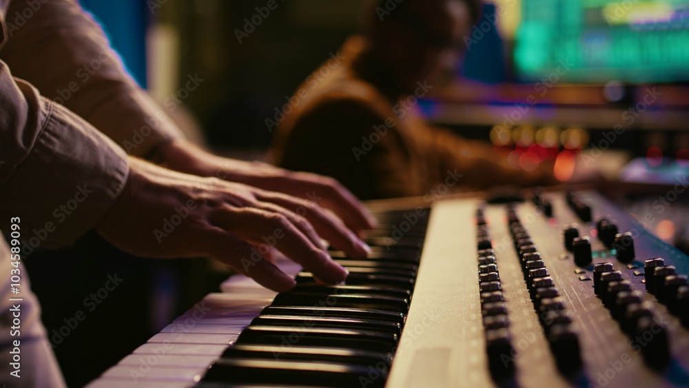 Fototapeta premium Musician composer playing midi controller synthesizer in professional studio, composing music on mixing console. Artist performing on piano electronic keyboard in control room. Camera B.