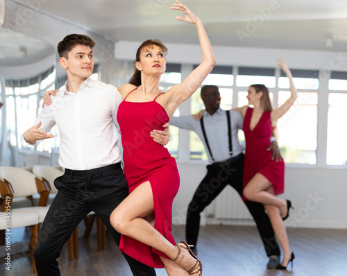 Happy man and woman in elegant red clothes enjoying ballroom dancing bachata in modern dance salon photo