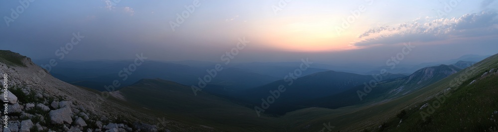 Fototapeta premium A panoramic view of a mountain range with a hazy sunset in the distance.