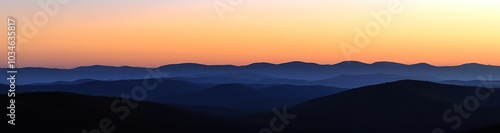 Silhouetted mountain range at sunrise with soft, hazy light and a blurred background.