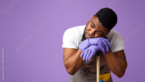 Exhausted Black Guy Leaning On Mop Handle, Resting Head On Hands Tired After Cleaning, Standing Over Pink StudioBackground With Free Space Done photo