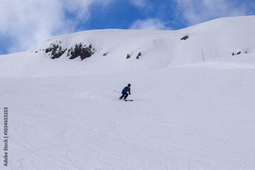 Young male skier in action skiing downhill in a European ski resort. Side view of skier descending in Les Menuires winter resort, France. Young male skier in action skiing downhill in a European ski resort. Side view of skier descending in Les Menuires winter resort, France.