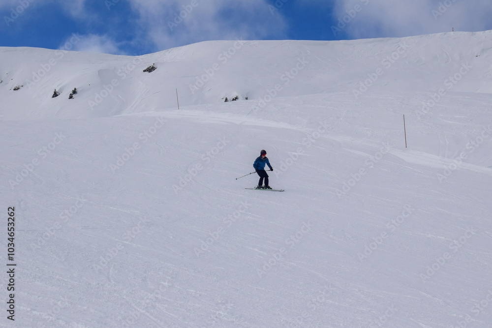 Young male skier in action skiing downhill in a European ski resort. Side view of skier descending in Les Menuires winter resort, France. Young male skier in action skiing downhill in a European ski resort. Side view of skier descending in Les Menuires winter resort, France.