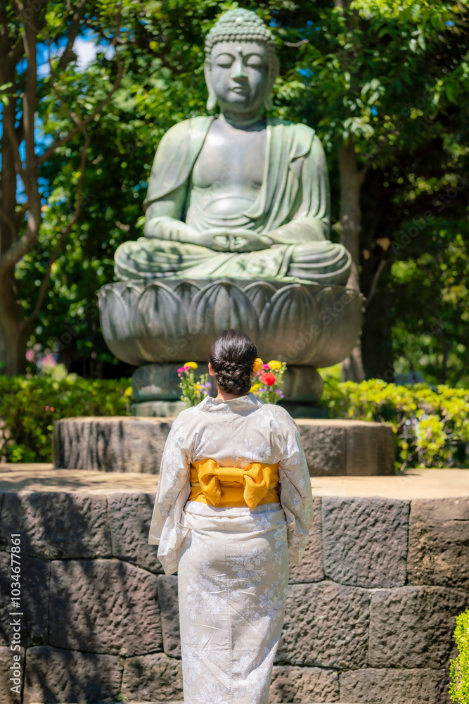 Unrecognizable young Latina woman in a kimono, standing in front of a large Buddha statue in Ueno Park, Tokyo, Japan, enjoying the serene atmosphere.