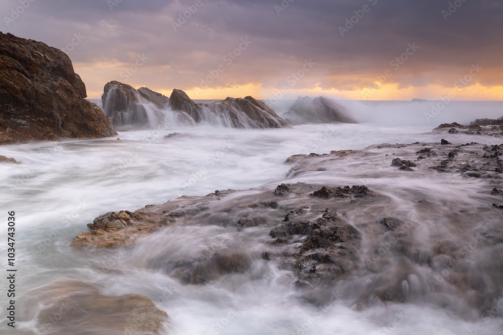 Waves crash over sea side rocks creating cascading waterfalls Waves crash over sea side rocks creating cascading waterfalls