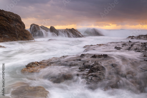 Waves crash over sea side rocks creating cascading waterfalls