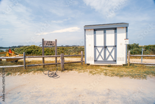 a free air pump for public use on the perimeter of a beach parking lot for people to fill their tires after driving on the beach, a small wooden shed and fence in the background