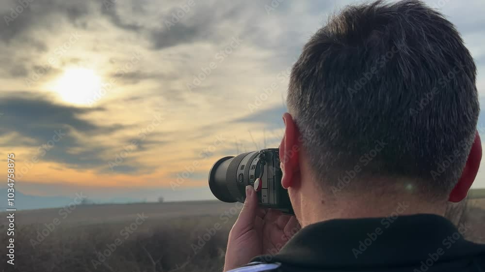 Back view of a male photographer using a DSLR camera to capture a stunning sunset scene over a serene landscape, showcasing the beauty of nature and the art of photography. Back view of a male photographer using a DSLR camera to capture a stunning sunset scene over a serene landscape, showcasing the beauty of nature and the art of photography.