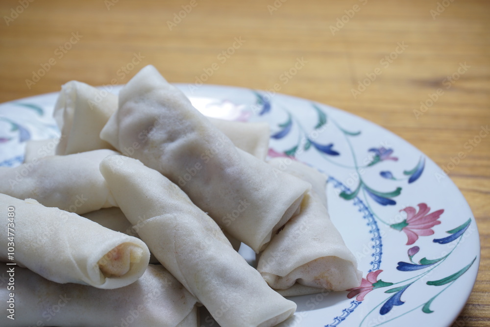 Heap of raw spring rolls(lumpia) on the plate. Frozen food on wooden tables. Heap of raw spring rolls(lumpia) on the plate. Frozen food on wooden tables.