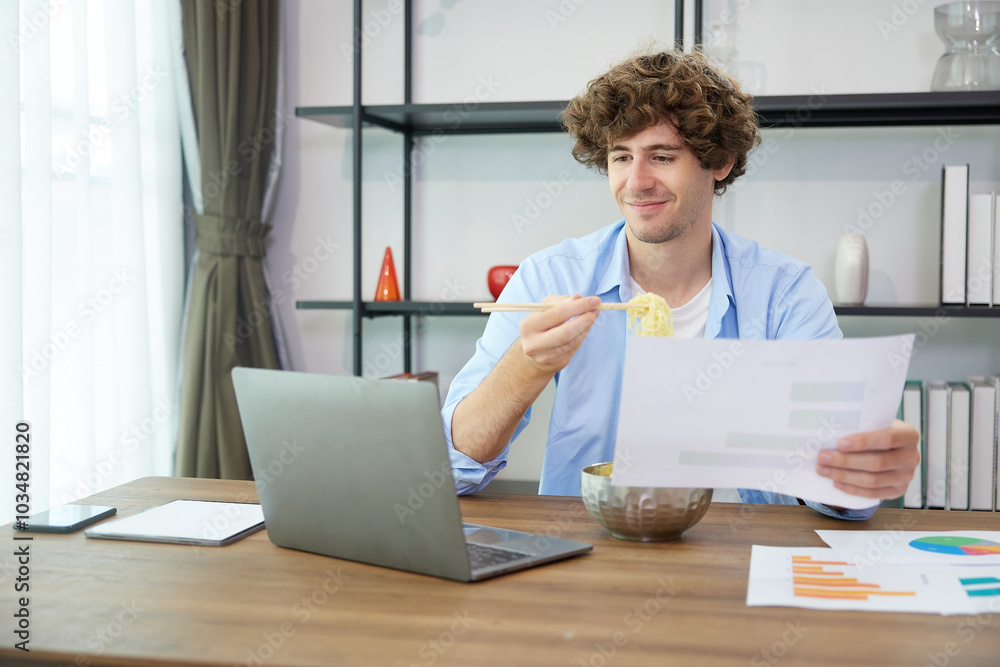 young man eating instant noodles and looking chart document paper at home young man eating instant noodles and looking chart document paper at home