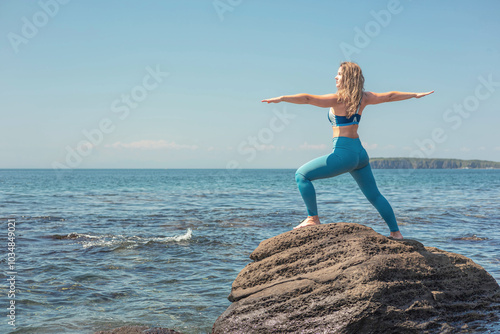 Woman practicing yoga in vira bhadrasana two warrior pose at cliff beach blue sea sky photo