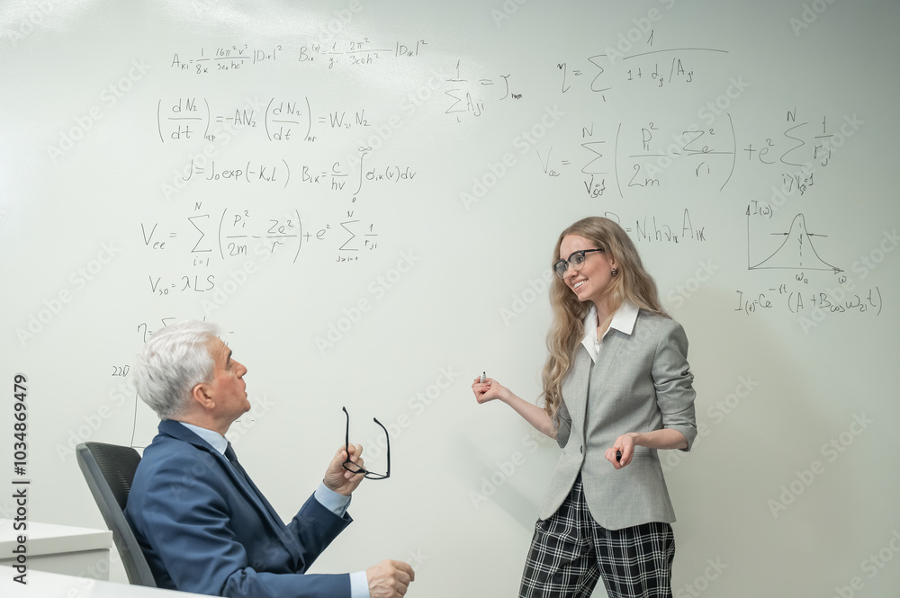 Fototapeta premium Female student answers a question from an elderly professor at a white board.