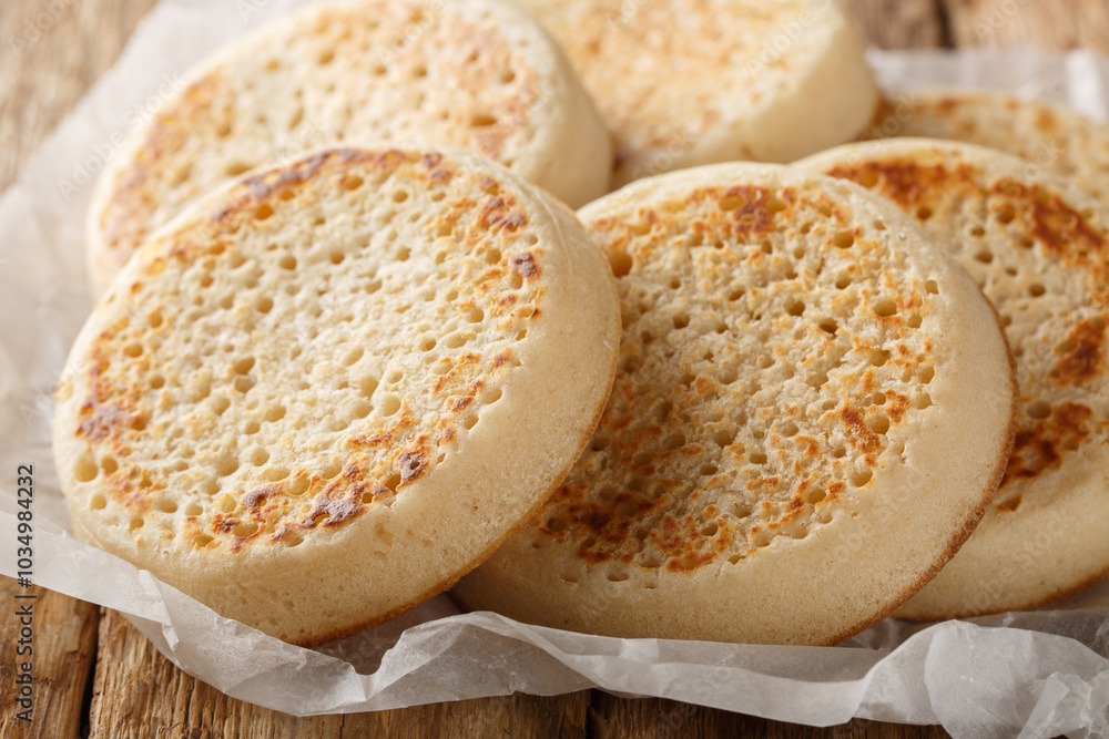 Fresh from the oven English Crumpets or porous bread close-up on parchment on an old table. Horizontal