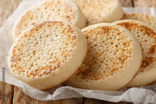 Obraz na płótnie Fresh from the oven English Crumpets or porous bread close-up on parchment on an old table. Horizontal w salonie