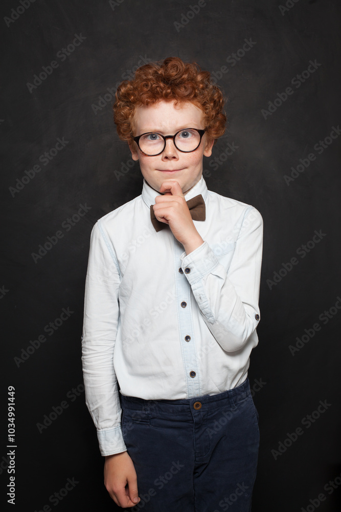 Handsome redhead young child boy shcool kid wearing white t-shirt thinking against black studio wall background Handsome redhead young child boy shcool kid wearing white t-shirt thinking against black studio wall background