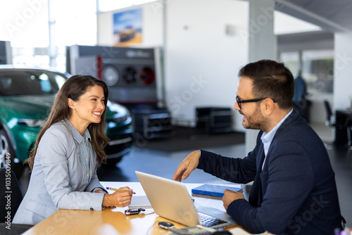 Smiling happy female manager car salesman in car dealership signing contract at table with male buyer in suit