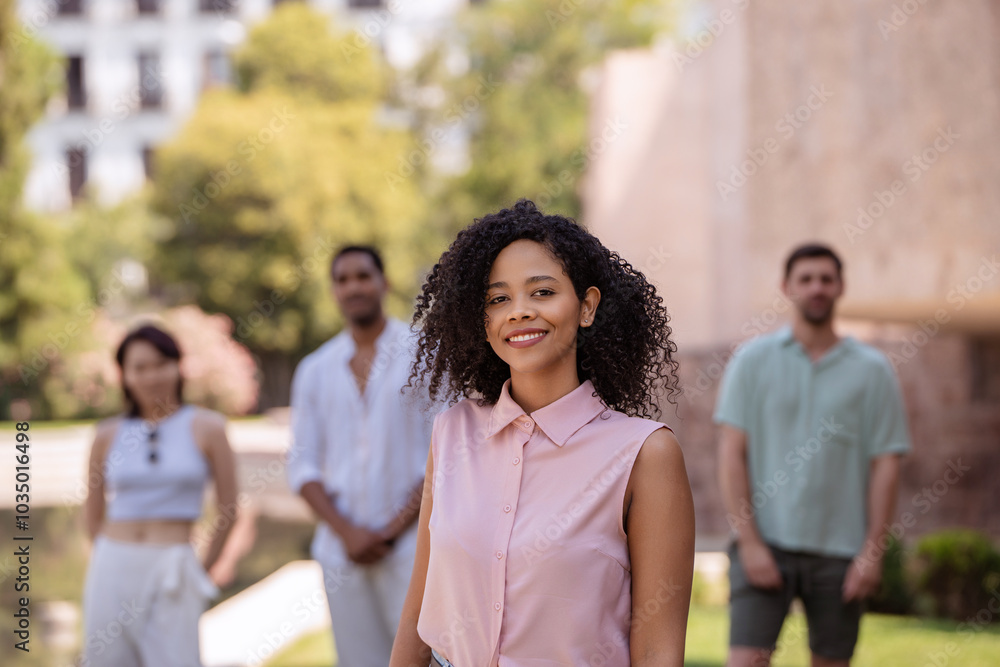 Young black woman is smiling in the foreground with three friends standing behind her out of focus Young black woman is smiling in the foreground with three friends standing behind her out of focus