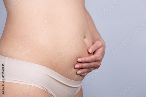 Close-up of the swollen belly of a woman resting her hand on it. Concept of woman, swelling and discomfort