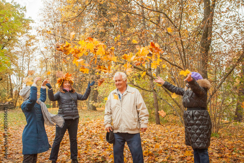 Senior grandma, mature muther and little child girl joyfully throwing autumn leaves at grandfather. Happy family having fun outdoor photo