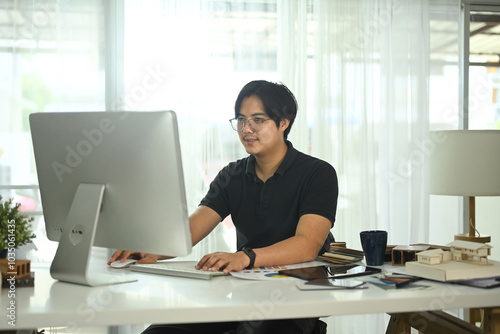 Handsome man working on project at desk surrounding with several architectural models and materials