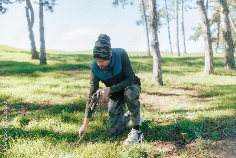 Man in Camouflage Gathers Firewood in a Forest Setting Man in Camouflage Gathers Firewood in a Forest Setting