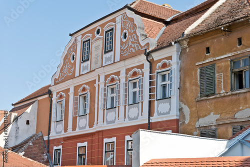 A colorful facade of a historic building in Sibiu, Romania. There is a plaque with Latin inscription and the name 