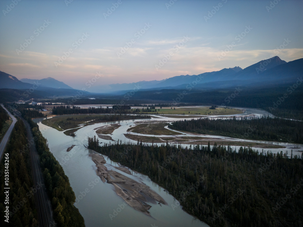 Aerial view of a serene sunset over majestic mountains and a winding river surrounded by lush forest, Golden, British Columbia, Canada. Aerial view of a serene sunset over majestic mountains and a winding river surrounded by lush forest, Golden, British Columbia, Canada.