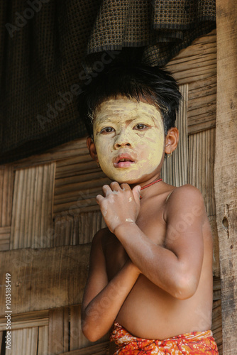 Bangladeshi tribal child standing on the doorway of his house with face makeup  photo