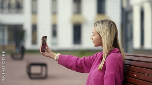 A young woman is happily capturing a vibrant selfie on her smartphone while sitting outdoors in nature