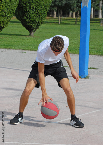 Boy playing basket ball on outdoors basket court.	