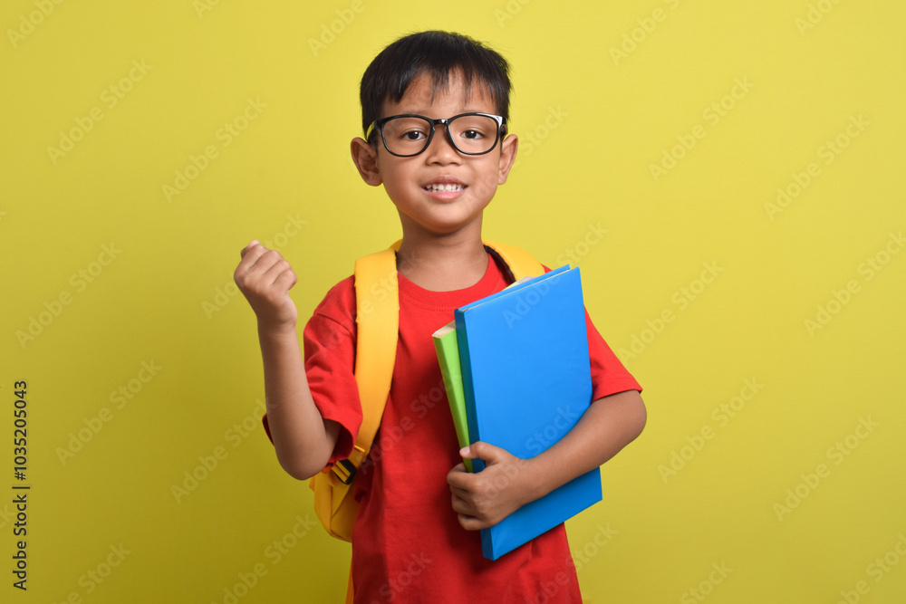 Cute and cheerful Asian boy smiling wearing backpack holding book gesturing showing victory sign isolated on yellow background. Time to study. Back to school Cute and cheerful Asian boy smiling wearing backpack holding book gesturing showing victory sign isolated on yellow background. Time to study. Back to school