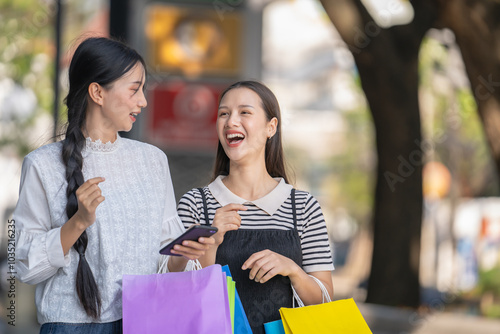 Two Asian women in modern clothes holding shopping bags walk outside a shopping mall...