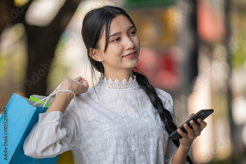 Asian woman in modern dress holding shopping bags walking outside a shopping mall.