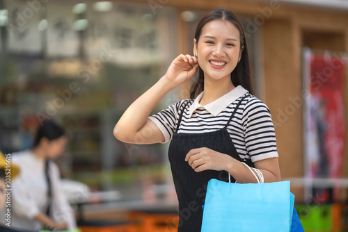 Happy Asian woman in modern dress holding shopping bags walking outside shopping mall