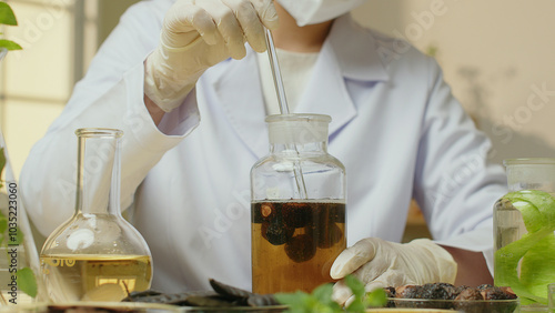 The scientist is using a glass rod to stir the soapberry solution contained in a cork bottle, surrounded by herbs such as honey locusts and soapberries scattered outside along with other solutions. photo