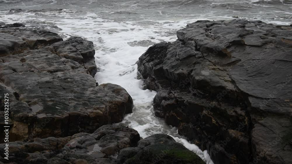 Waves crash against rugged coastal rocks in an overcast, moody seaside landscape Waves crash against rugged coastal rocks in an overcast, moody seaside landscape