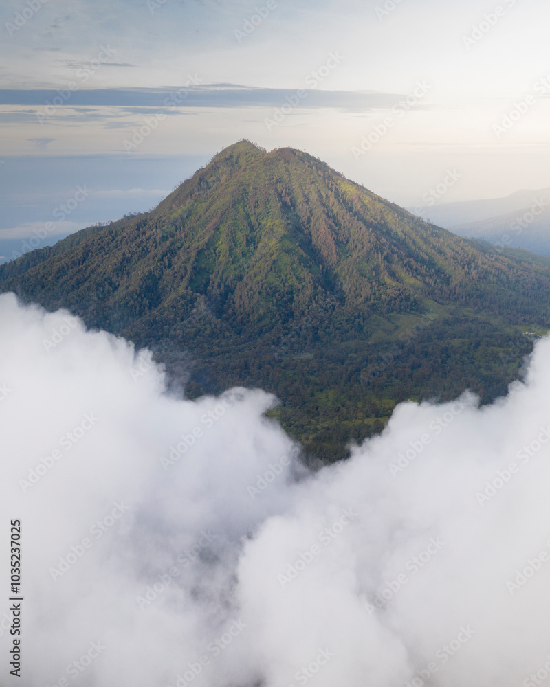 Aerial view of a majestic volcano surrounded by lush greenery and clouds at sunset, Licin, Banyuwangi, East Java, Indonesia.