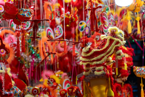 A close up shot of multiple red dragon masks with fur and decorative details. Colorful plastic toys and paper lanterns in the background