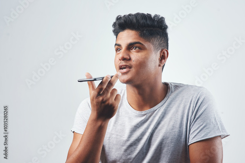 Indian man, discussion and speaker with phone for audio message, chat or conversation on a white studio background. Young, male person or gen z model with mobile smartphone, loudspeaker or voice note photo