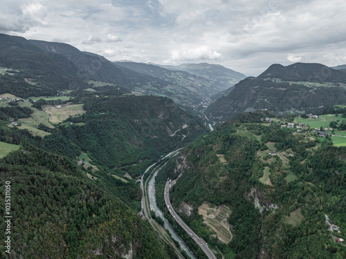 Aerial view of a serene valley surrounded by majestic mountains and lush forests with a winding road, Vols am Schlern, Italy. photo