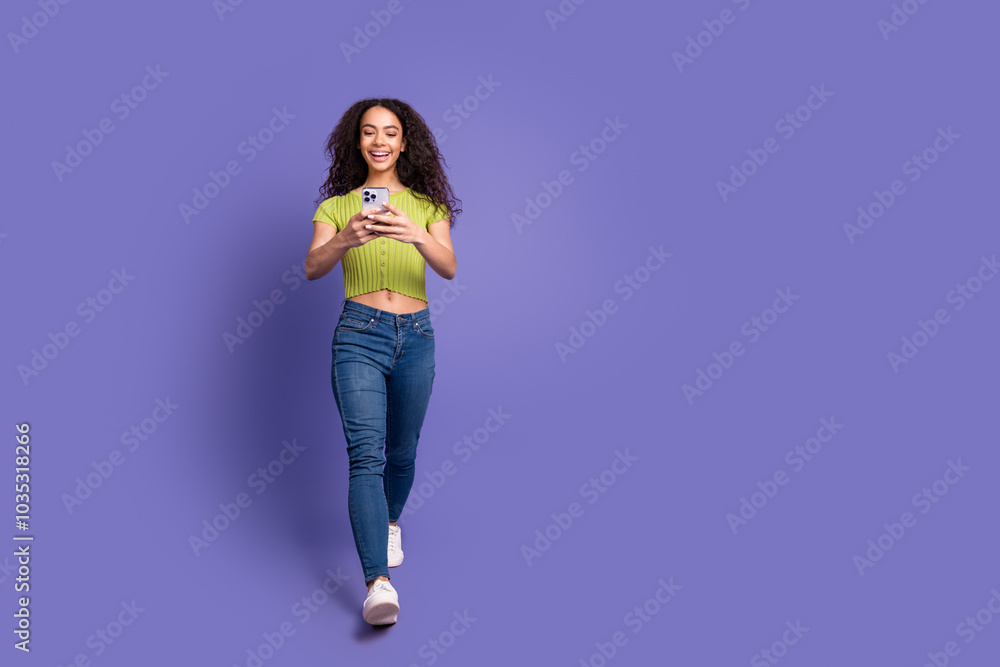 Full size photo of pretty teen girl hold gadget walking wear trendy green outfit isolated on purple color background Full size photo of pretty teen girl hold gadget walking wear trendy green outfit isolated on purple color background