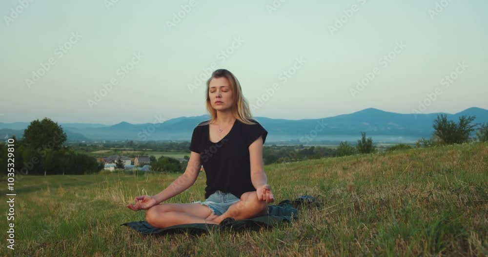 Relaxed peaceful caucasian woman meditating on a green meadow with high mountains in the background with animated text word reflection visualization behind her back. Yoga Practice, self-care Relaxed peaceful caucasian woman meditating on a green meadow with high mountains in the background with animated text word reflection visualization behind her back. Yoga Practice, self-care