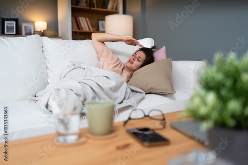 Woman sleeping on couch at home resting wrapping in plaid feeling bad symptoms. Girl suffering from seasonal flu or cold. Feel unhealthy with influenza. Tired exhausted workaholic becoming ill, sick. photo