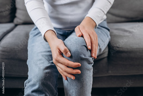 Young woman suffering on leg, pain knee from disease chronic, hand massage rubbing joint injury, female hurt or sore sitting on couch at home. Body arthritis muscles stiff problem. Health care people