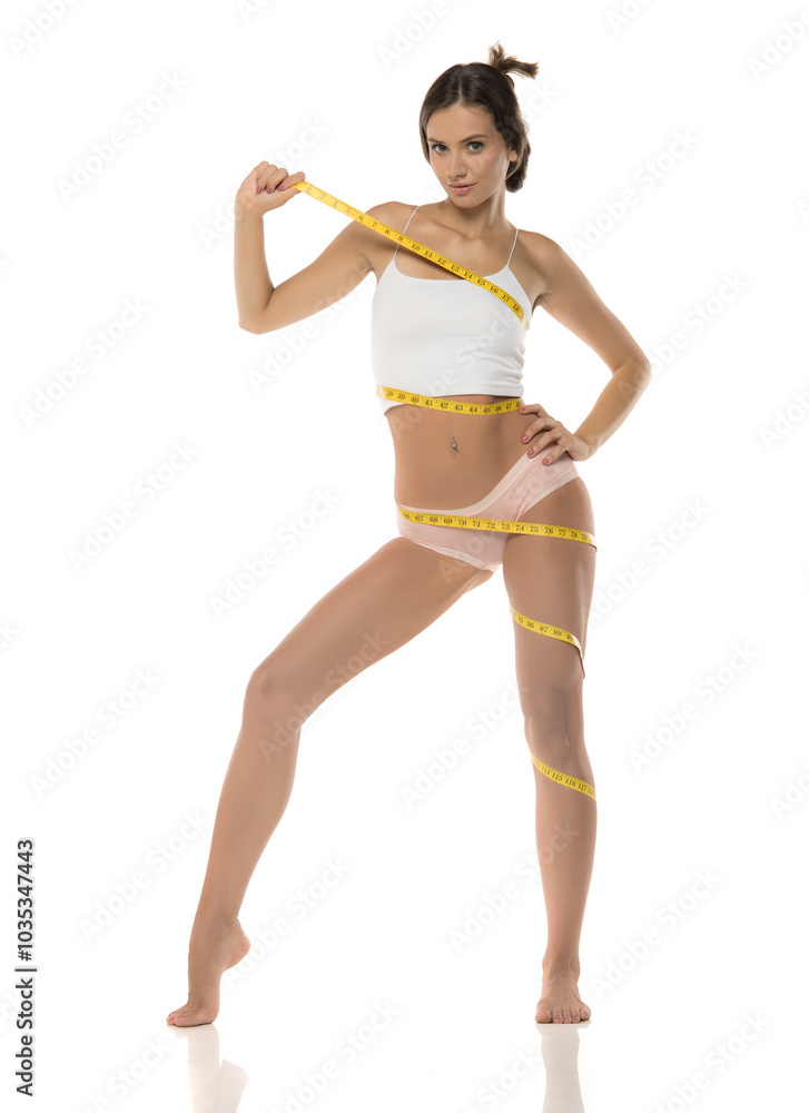 Young woman measure the whole body with a tape on white studio background. Young woman measure the whole body with a tape on white studio background.