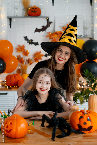 A happy family is getting ready for Halloween. Mother and child daughter in carnival costumes at home in the kitchen having fun scaring each other and laughing