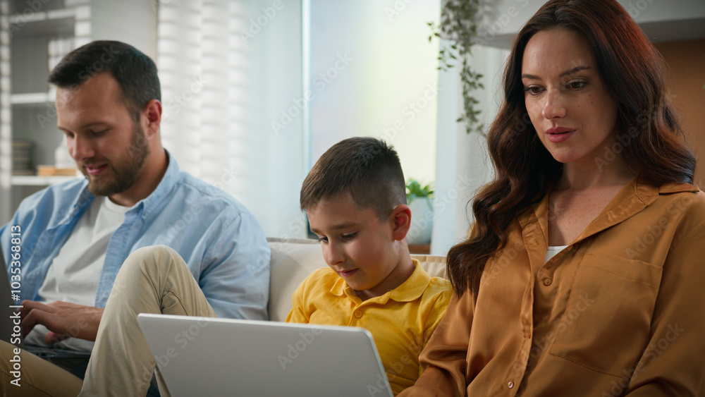 Caucasian family man woman father mother parents working remote online on laptop kid boy child son playing on mobile phone smartphone on couch home gadget addiction modern technology weekend together